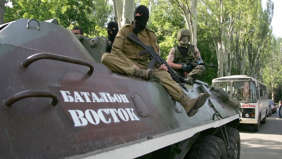 Vermummte Separatisten mit Gewehern auf einem Panzer.