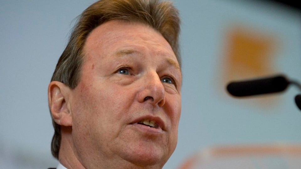 Porträtfoto von Peter Zwick, rechts seitlich der Schatten eines Mikrofons, im Hintergrund verschwommen das orange CVP-Logo.
