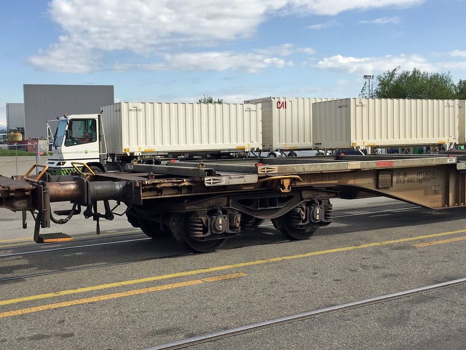 Leerer Güterwagen, im Hintergrund Transportlastwagen mit Container