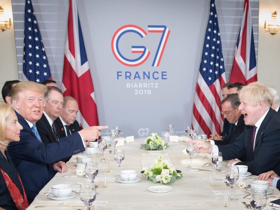 Trump und Johnson mit Entourage lachen am Frühstückstisch.