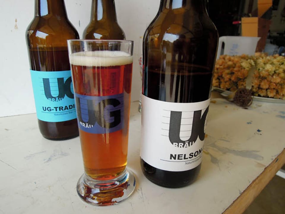 Ein gefülltes Bierglas, umrahmt von Bierflaschen mit spezieller Etikette.