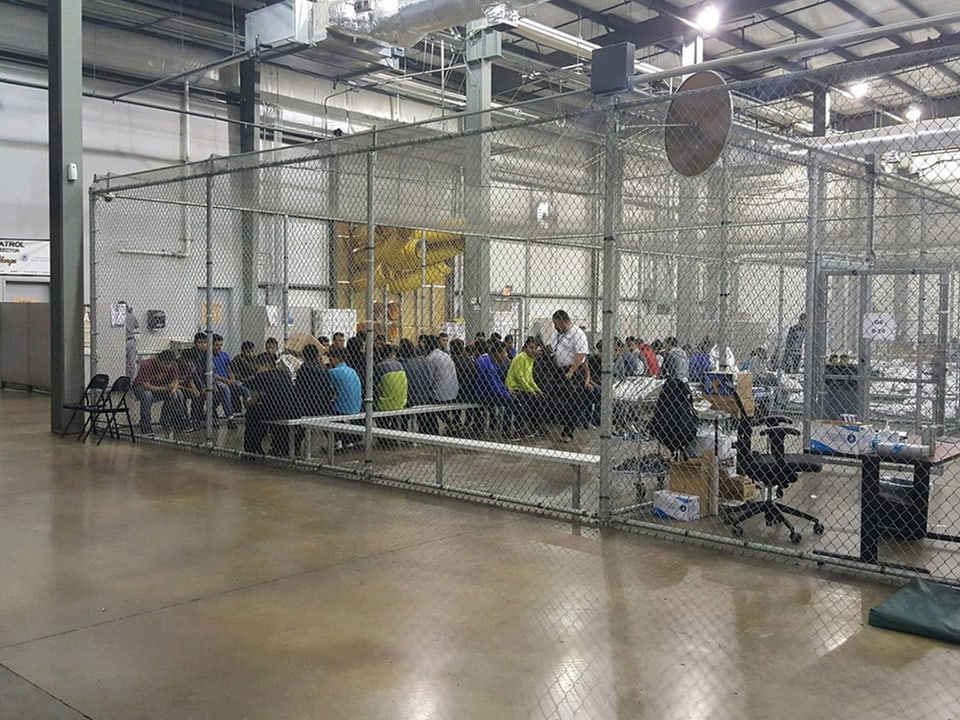 Kinder sitzen an einem Tisch hinter einem Gitter.