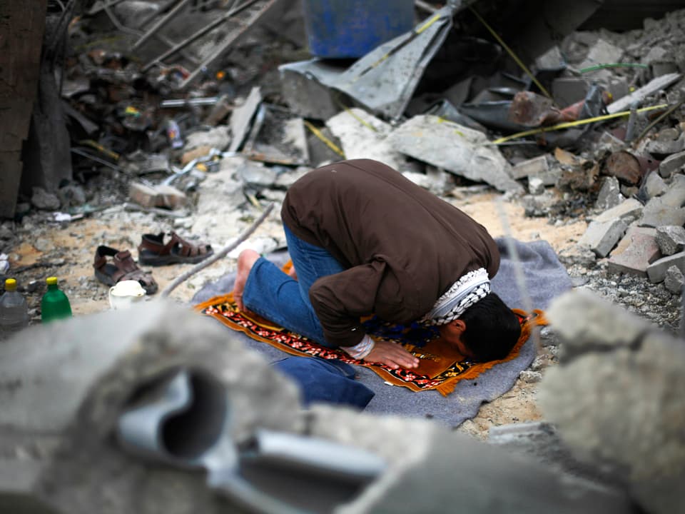 Mann auf Gebetsteppich inmitten von Trümmern. 