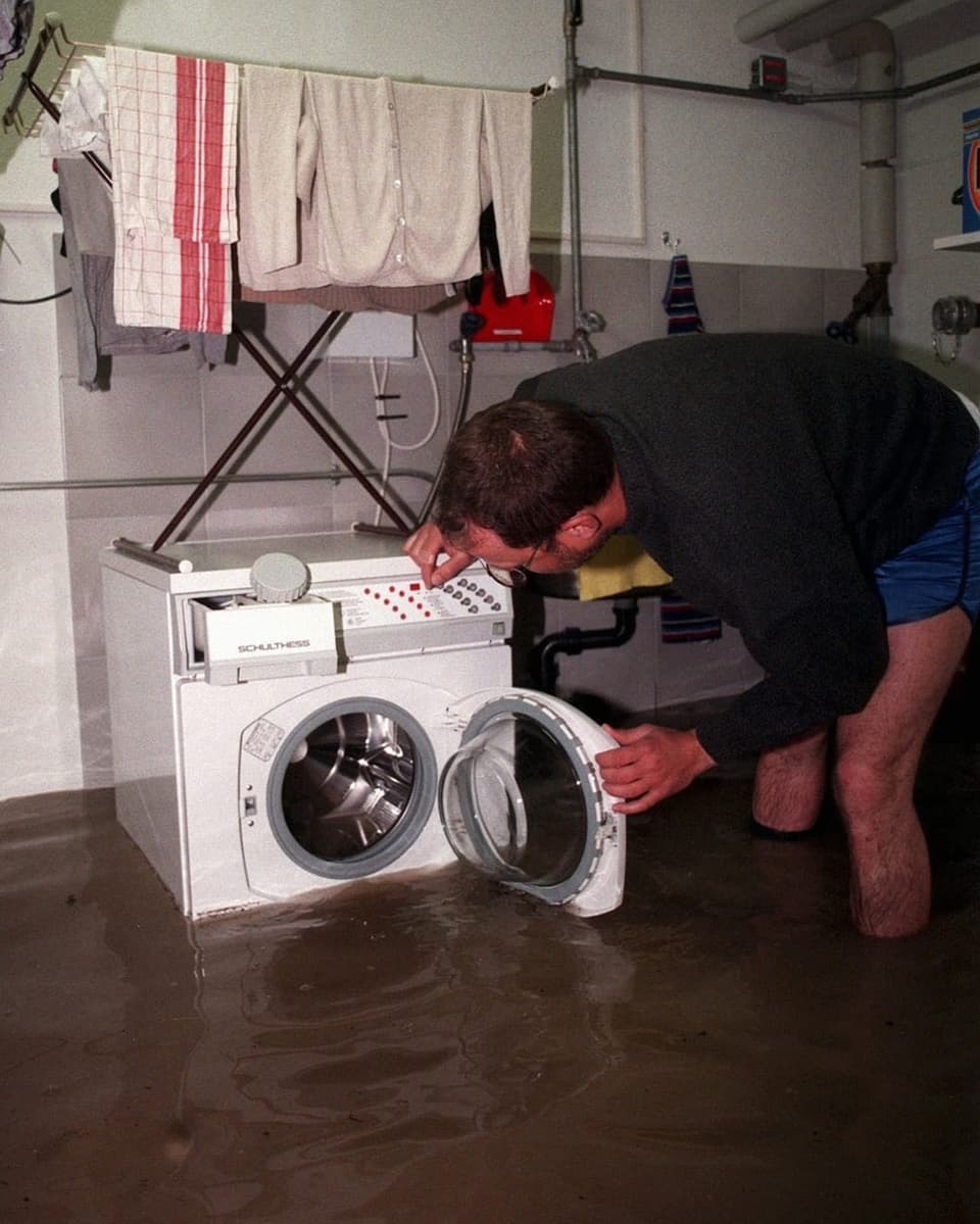Mann beugt sich über eine Waschmaschine in einem überschwemmten Keller.