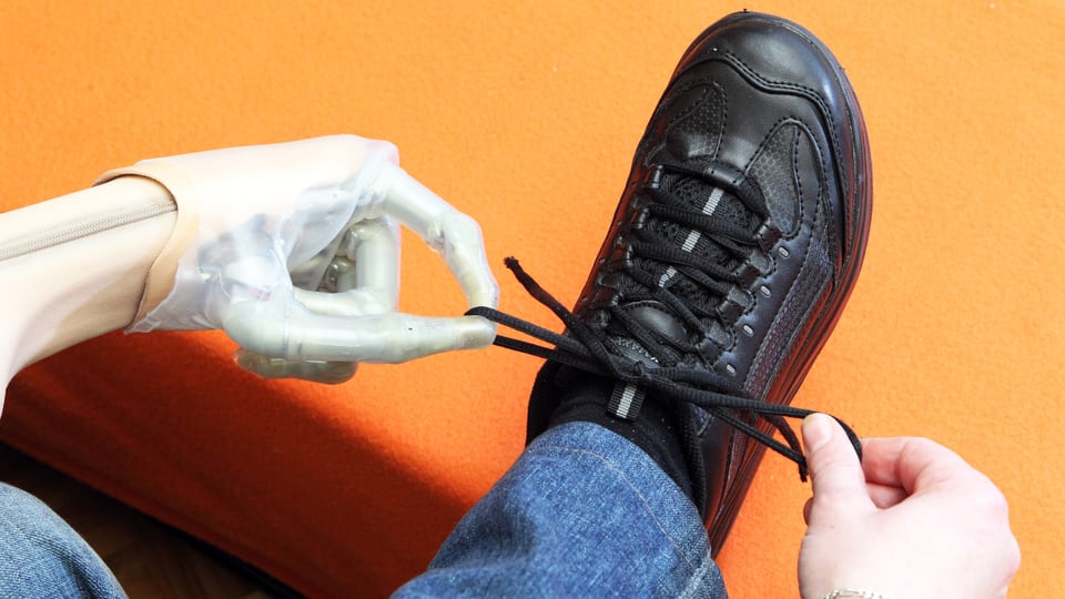 Eine Hand und eine Handprothese beim Binden eines Schuhbändels.