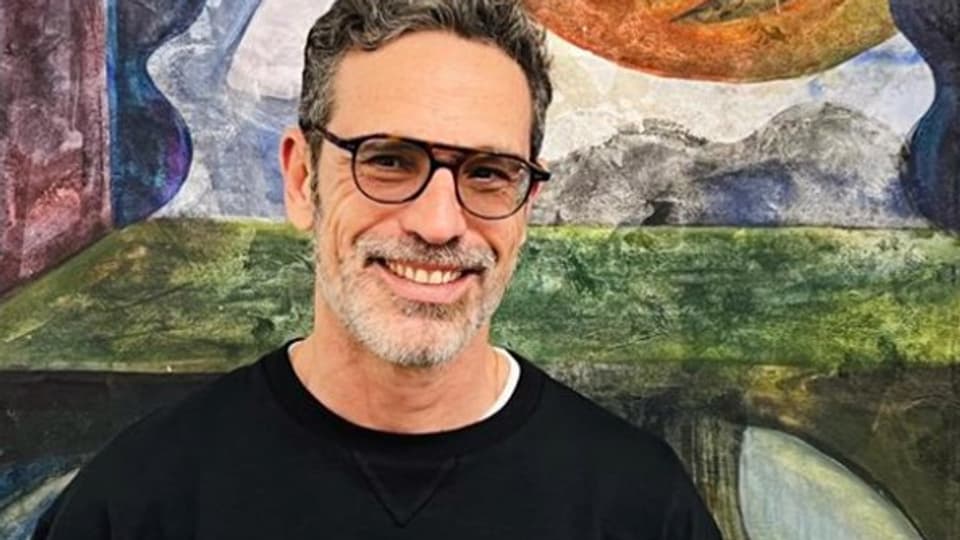 Ein Mann mittleren Alters mit Brille lächelt.