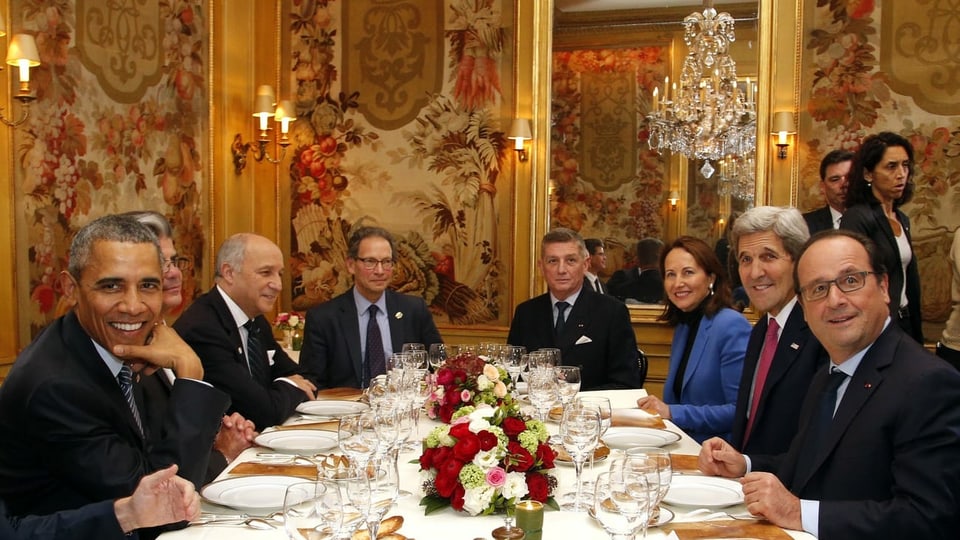 Männer und eine Frau sitzen rund um einen festlich gedeckten Tisch.