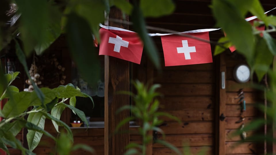 Schweizer Fähnchen hängen vor einer Holzfassade.