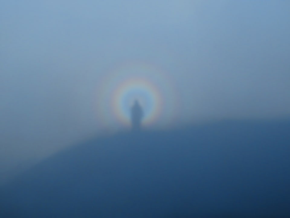 Das Bild ist überzogen von dichtem Nebel. Das Bild des Fotographen wirf einen Schatten auf den Nebel. Um den Schatten liegen konzentrische Kreise aus Regenbogenfarben.