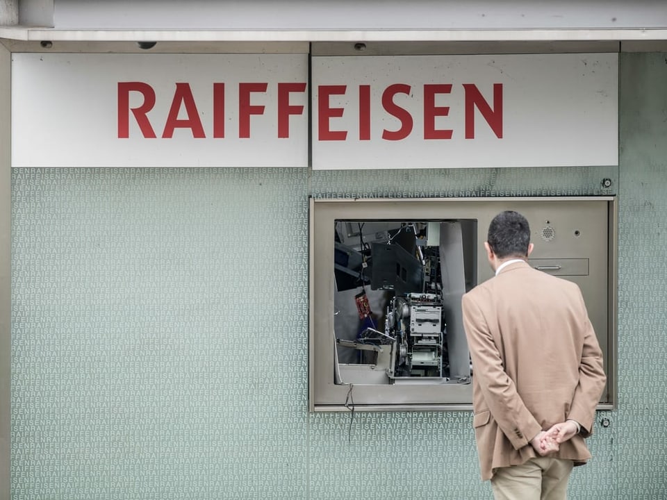 Ein Mann steht vor einem gesprengten Bancomat der Raiffeisen-Bank