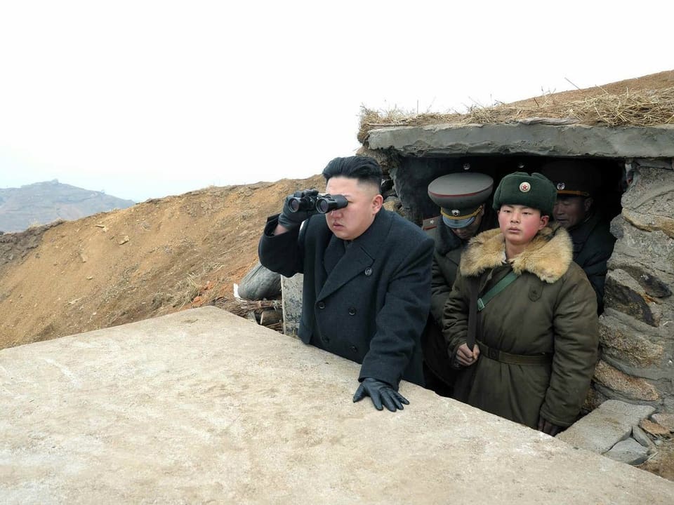 Kim Jong Un mit Feldstecher in einer Hütte, er schaut in die Ferne.