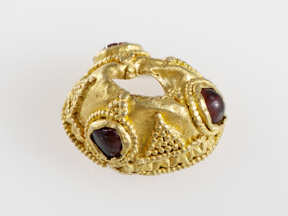 Ein goldener Kopf für eine Gewandnadel, verziert mit drei Edelsteinen.