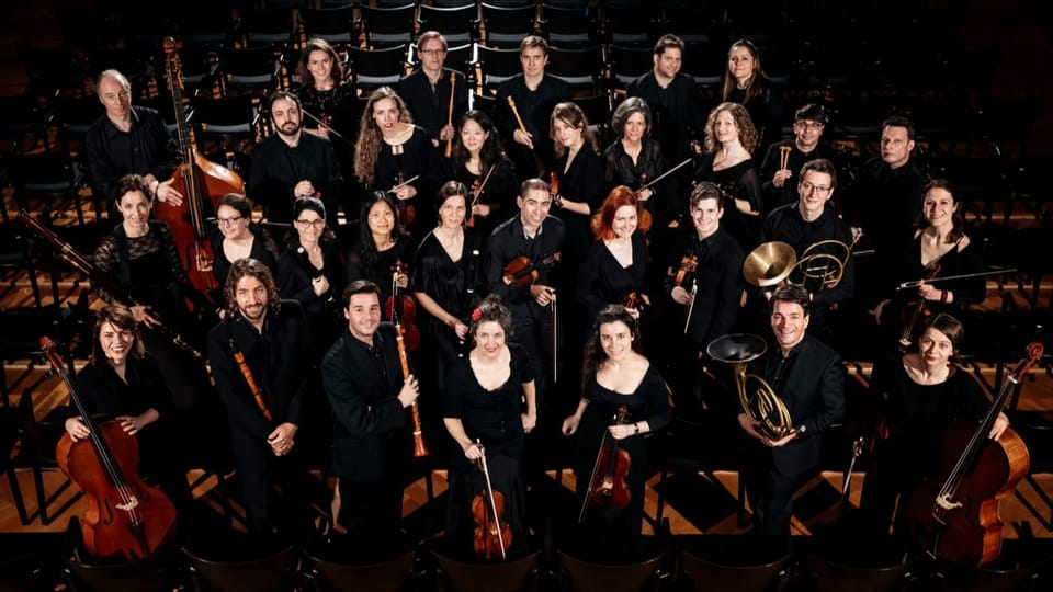 Ein Orchester in schwarz gekleidet von oben fotografiert.