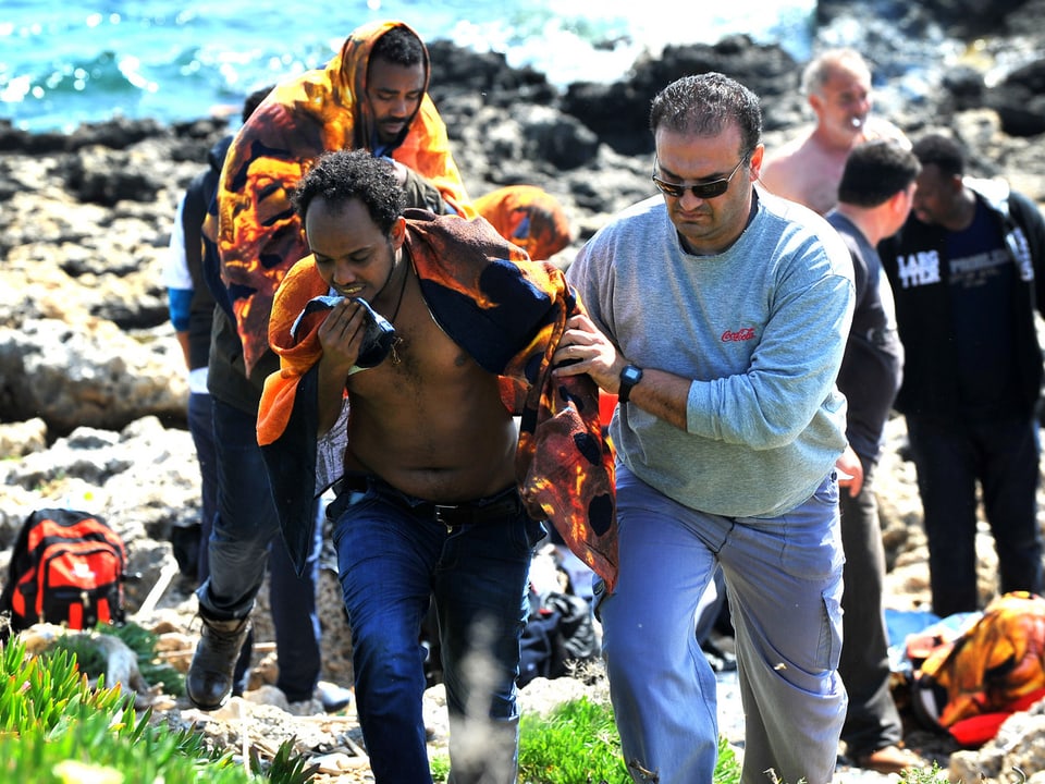 Ein Grieche hilft einem erschöpften Flüchtling, den Hang hinauf zu gehen.