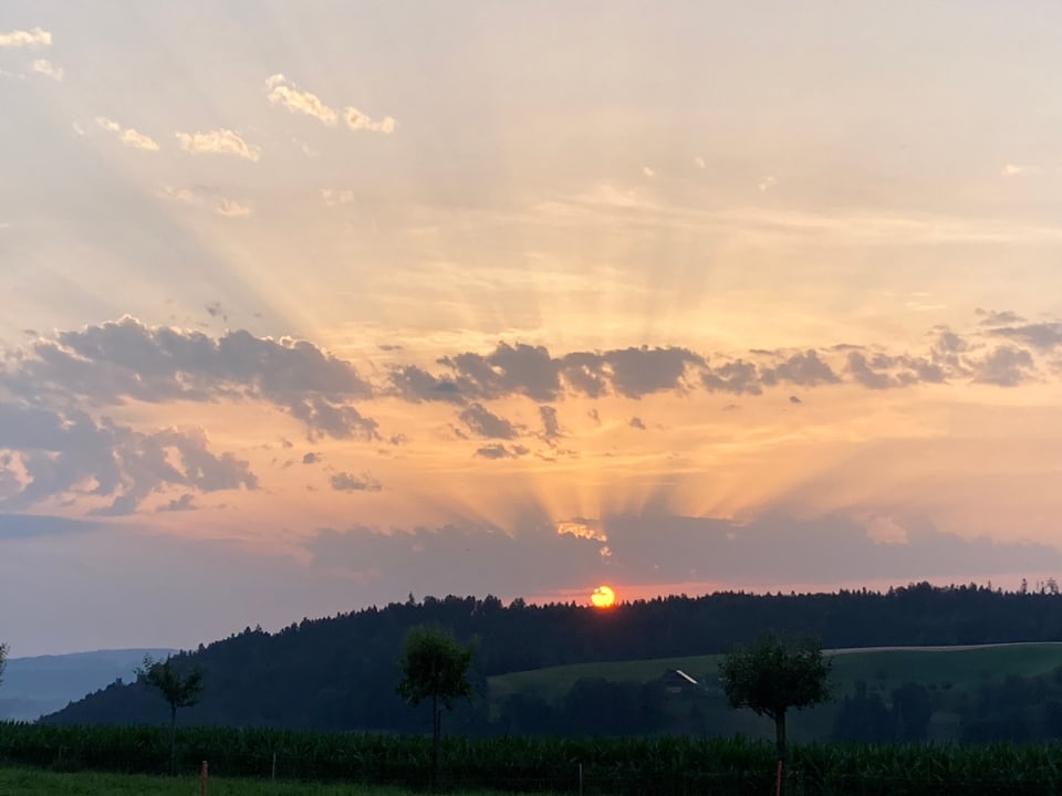 Die Sonne geht hinter einem Hügel auf, wenige Wolken am Himmel.