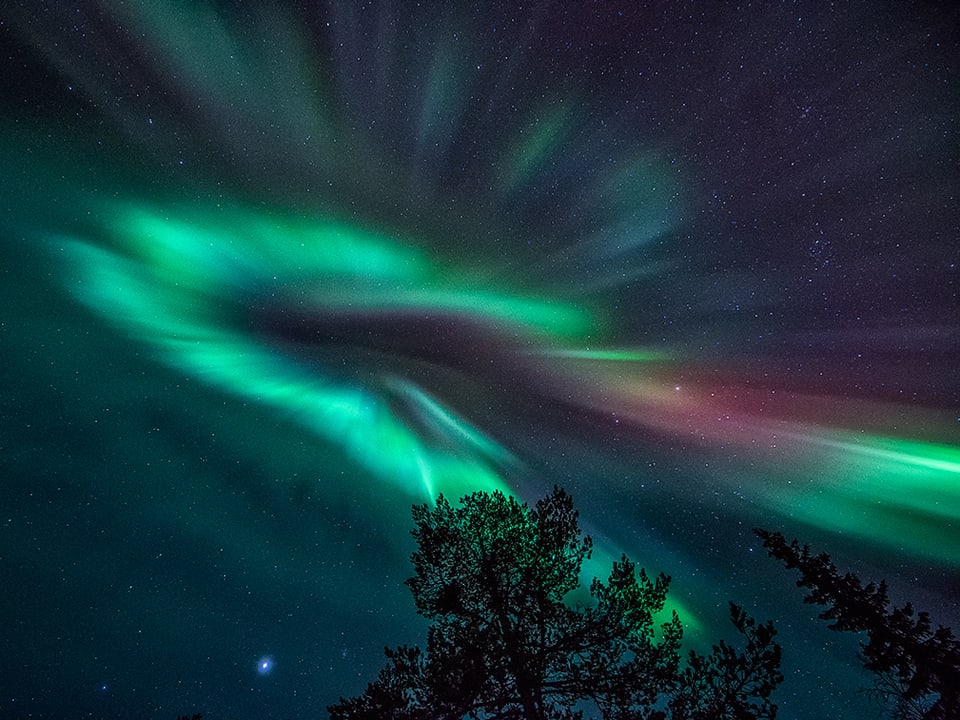 Dunkler Nachthimmel mit kreisförmigem Polarlicht in grün-blau. 