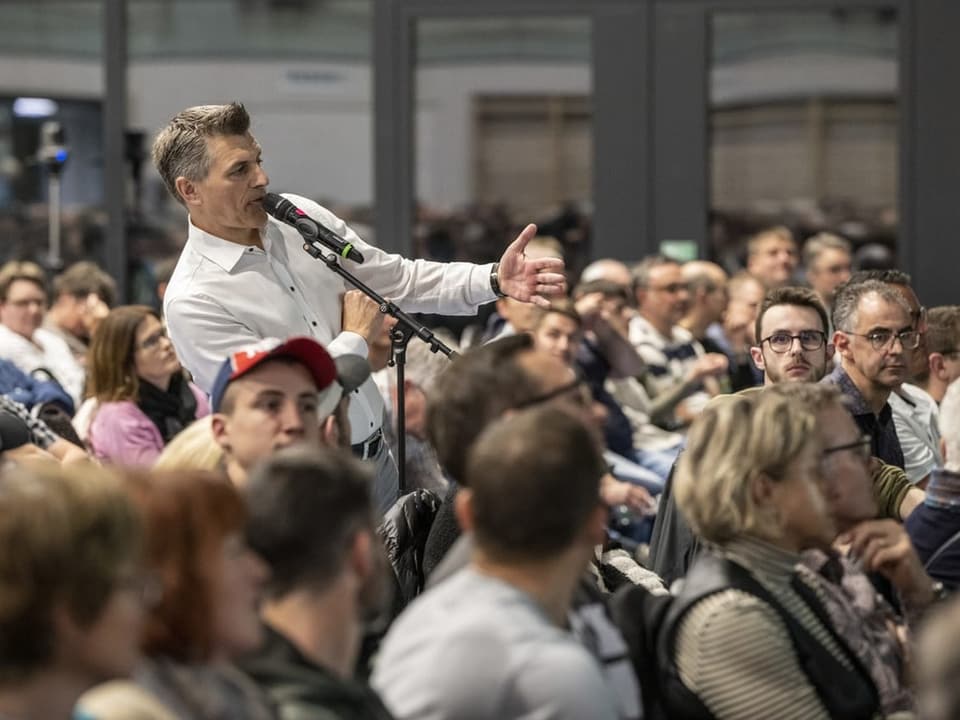 Mann spricht ins Mikrofon vor Publikum bei einer Veranstaltung.