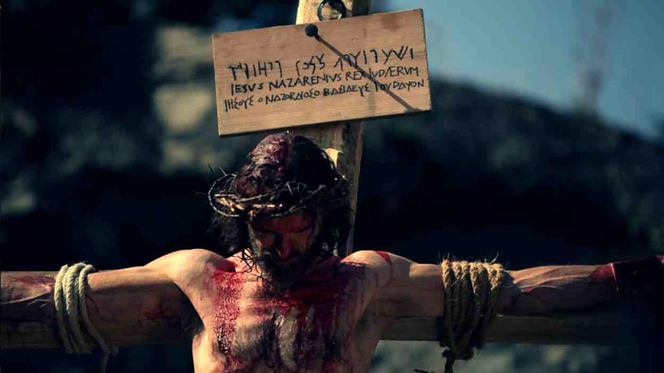 Jesus, der mit Seilen ans Kreuz gebunden ist, lässt den Kopf hängen. 
