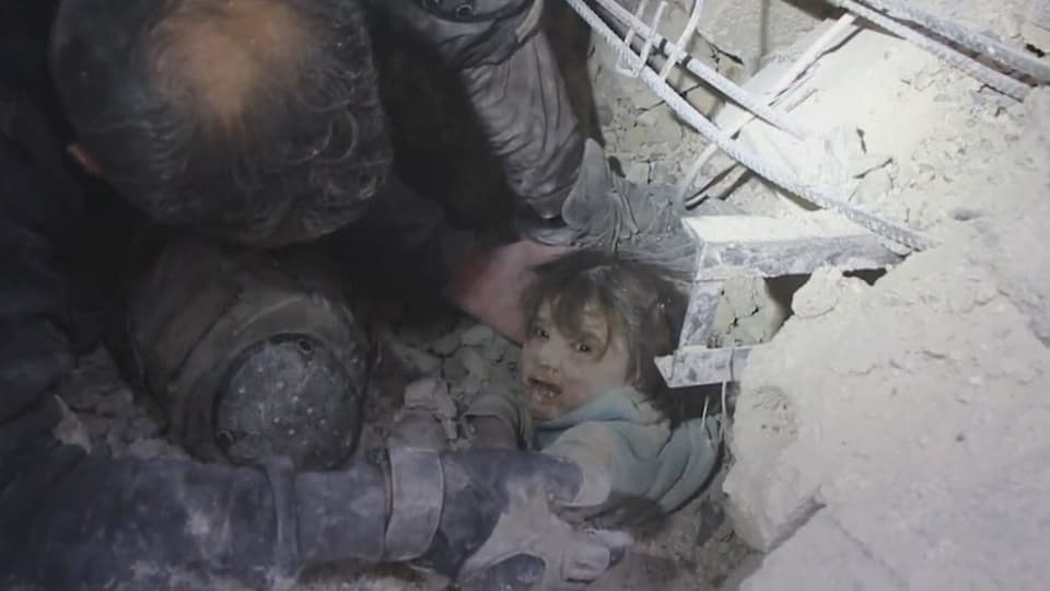 Kleines Mädchen blickt in die Kamera, von Staub bedeckt, Hände ziehen sie aus den Trümmern