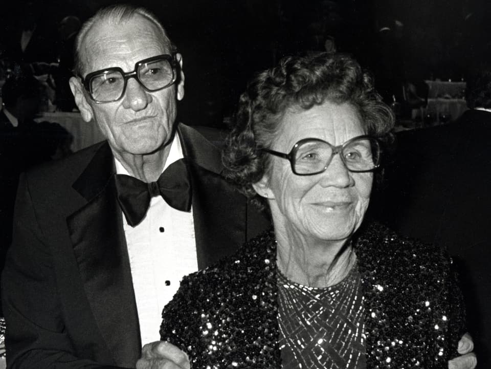 Reynolds Eltern im Anzug und Glitzerkleid mit Hornbrille.