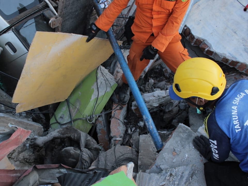 Zwei Rettungkräfte brgen einen überlebenden Mann aus den Trümmern.