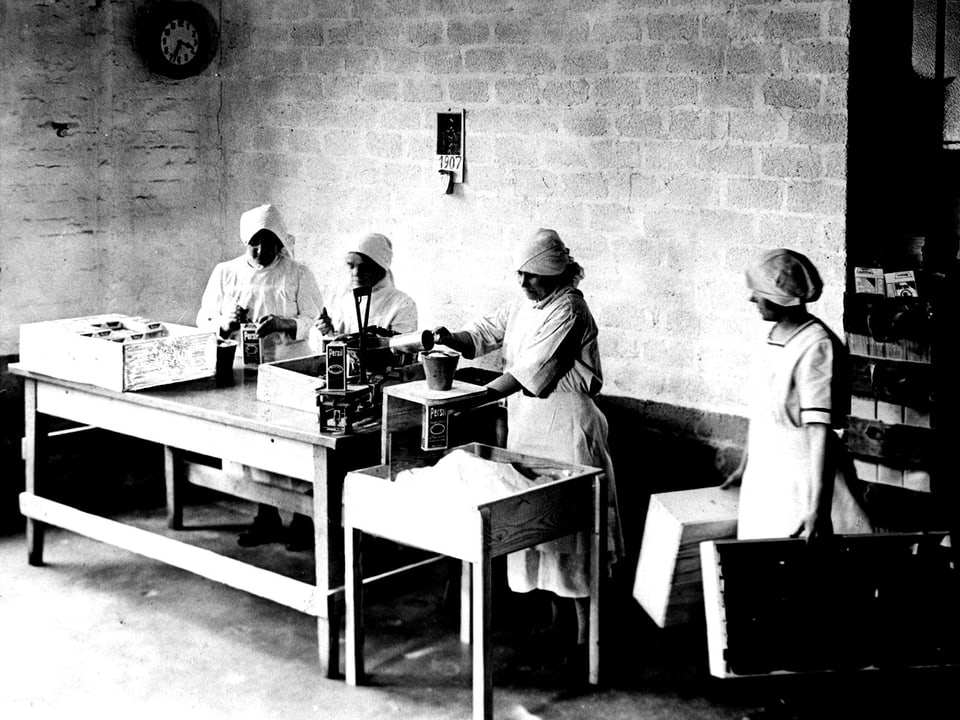 Arbeiterinnen stehen im Jahr 1907 an Einfüllmaschinen, mit denen Waschmittel abgefüllt wird. 