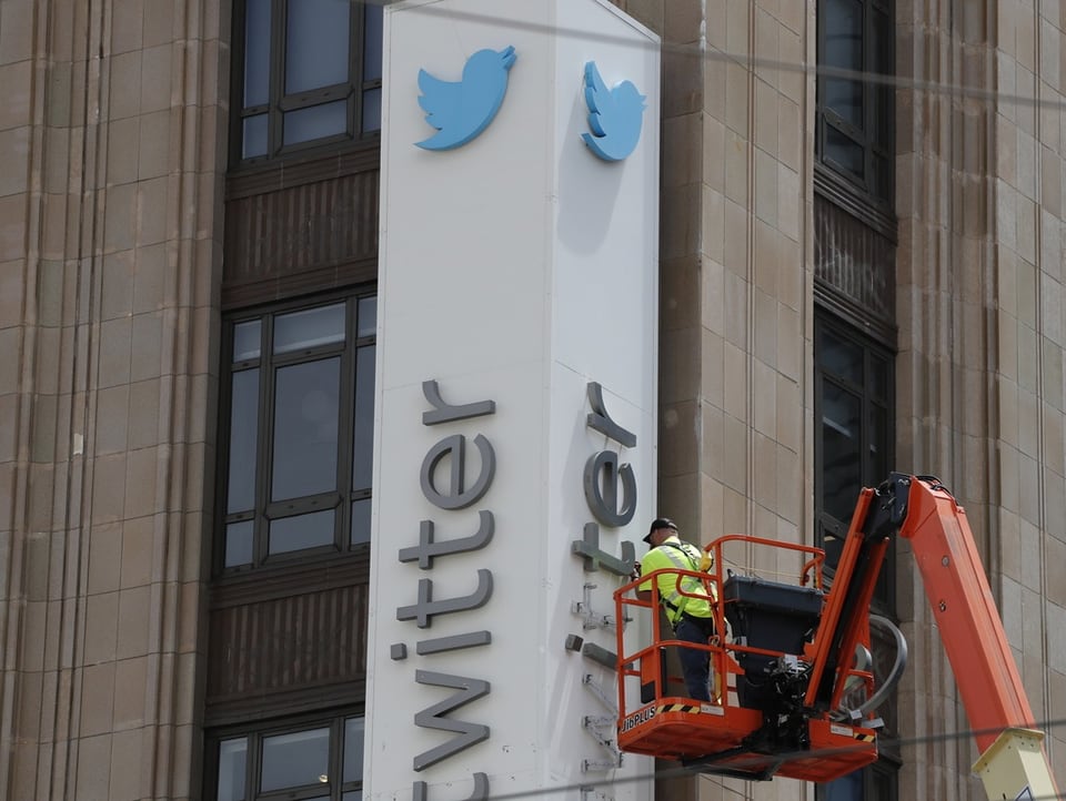 Eine Person auf einer Hebebühne entfernt die Schrift «Twitter» von einem Gebäude.