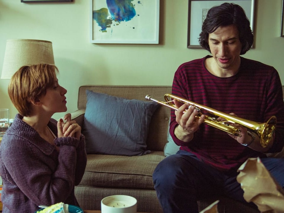 Man with a trumpet on a sofa, a woman kneeling on the floor next to him.