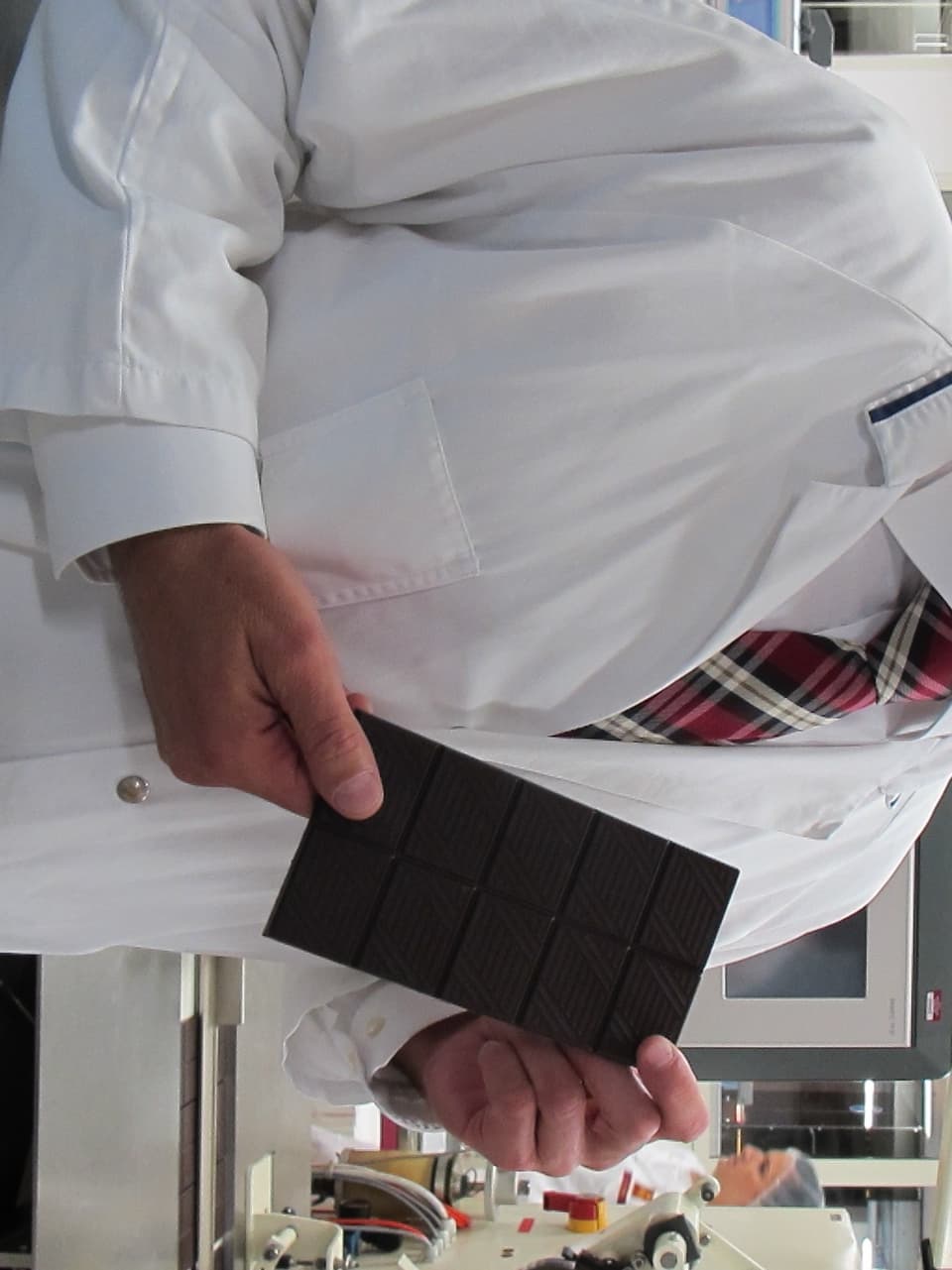 Mitarbeiter der Chocolat Frey steht in der Produktionshalle mit einer Tafel Schokolade in der Hand.