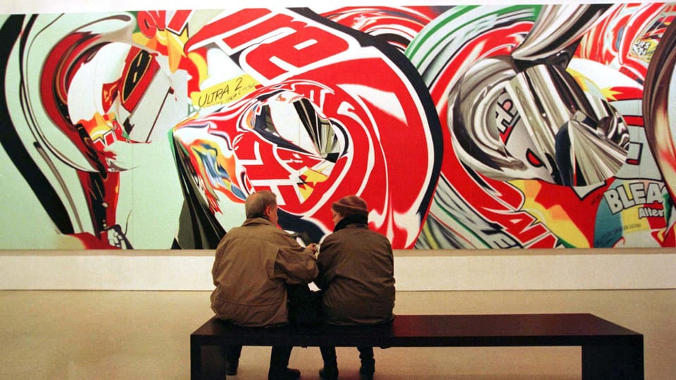 Zwei Personen sitzen auf einer Museumsbank. Im Hintergrund eine raumfüllende, collageartige Malerei. 