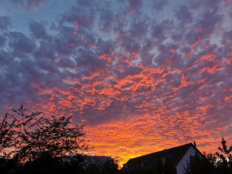 Sonnenuntergang mit rotgefärbten Wolken über einem Dach.
