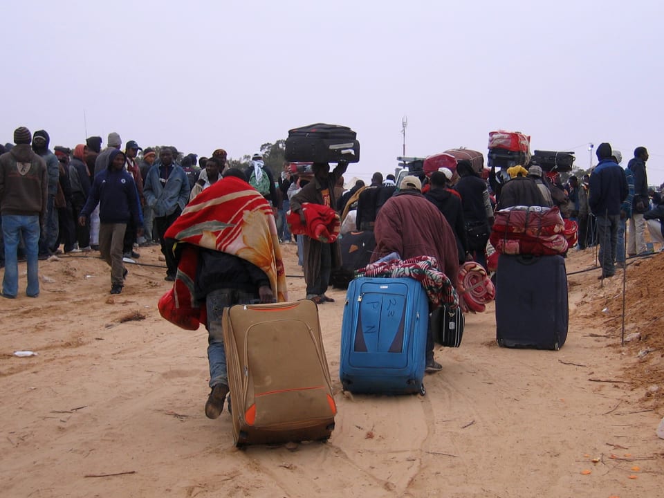 Flüchtlinge ziehen ihre Rollkoffer durch den Sand