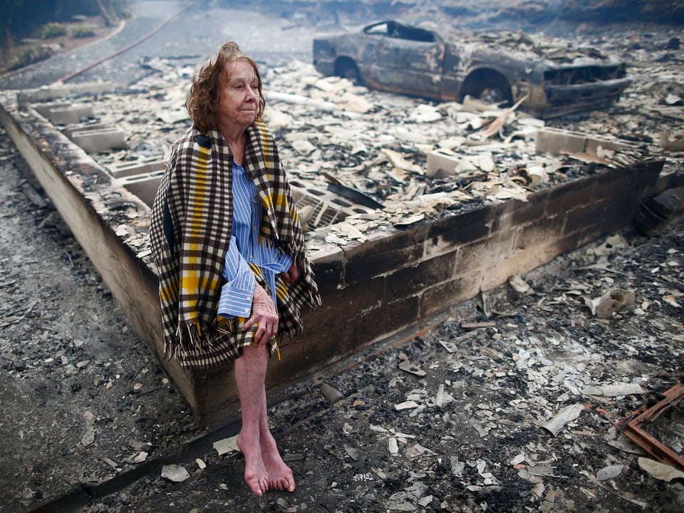 Eine Anwohnerin sitzt auf der Grundmauer ihres niedergebrannten Hauses. 
