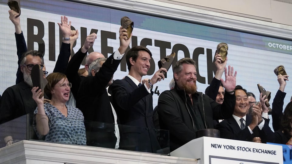 Mehrere Personen jubeln mit hochgehaltenen Birkenstock-Sandalen auf Podium an der New Yorker Börse