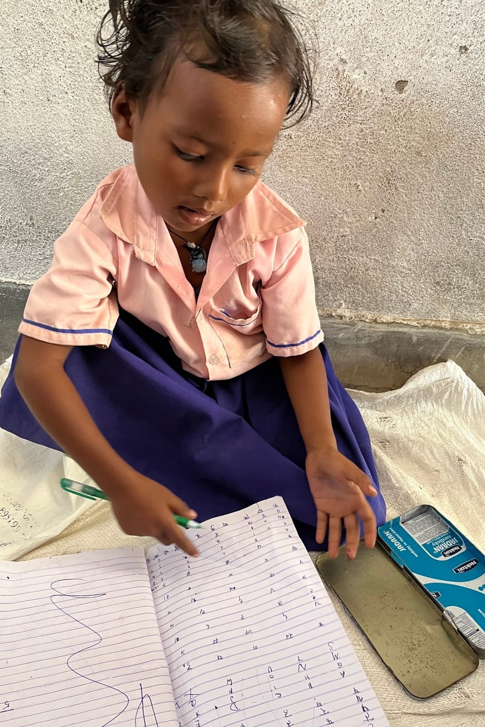Ein kleines Mädchen in Schuluniform sitzt am Boden und spielt Schule.