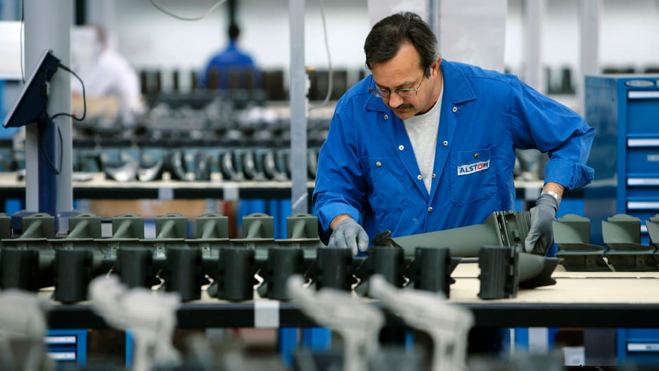 Ein Arbeiter von Alstom mit blauem Arbeitskittel an einem Laufband in der Fabrik in Birr. 