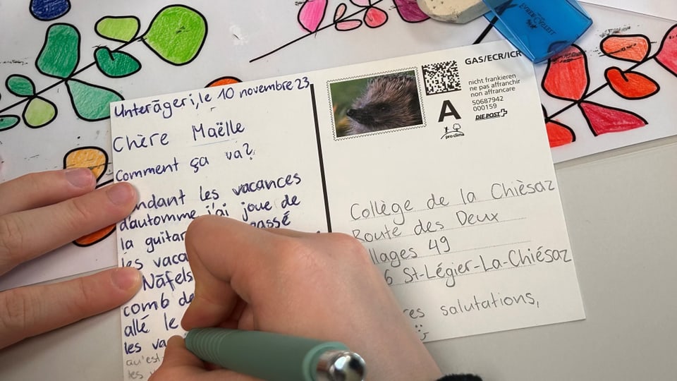 Ein Kind schreibt eine Postkarte auf französisch.