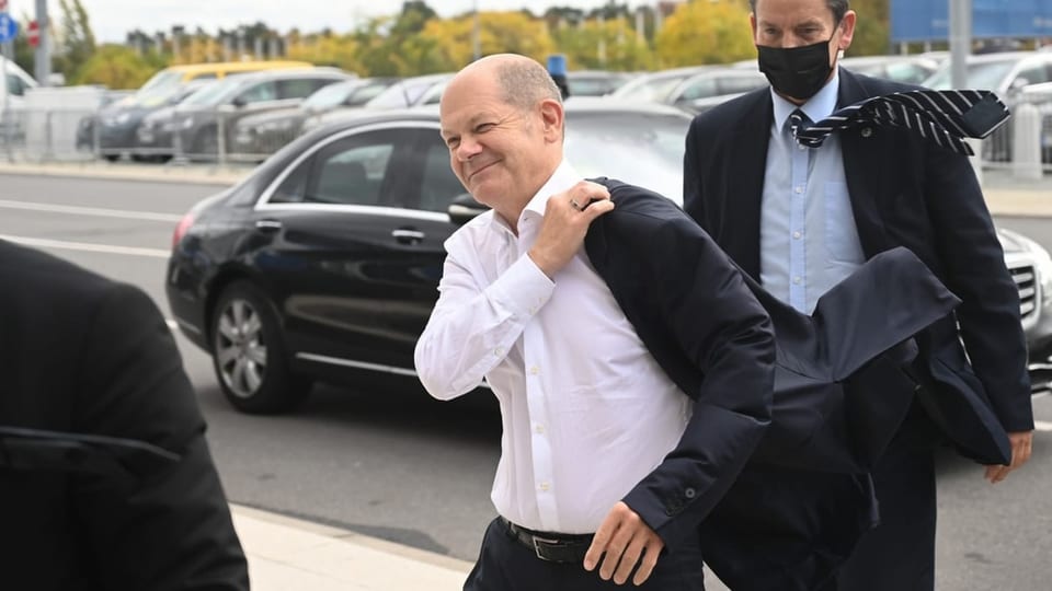 Ein gutgelaunter Mann mit weissem Hemd hält seine Jacke mit der rechten Hand.