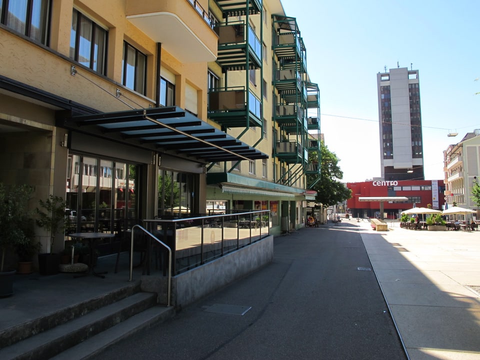 Restaurant Terrasse mit Stühle neben einem leeren Platz, im Hintergrund ein Hochhaus