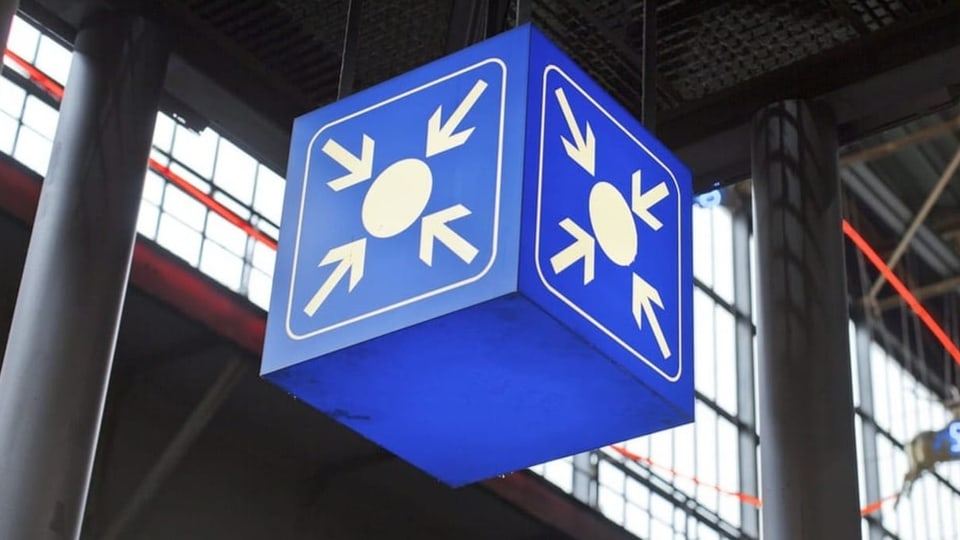 Ein blauer Kubus mit «Treffpunkt»-Symbol hängt in einem Bahnhofsgebäude