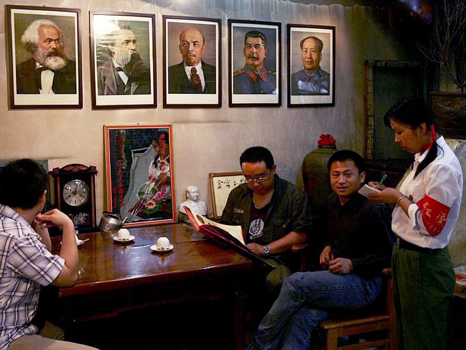 Eine Kellnerin, die wie eine rote Gardistin angezogen ist, nimmt eine Bestellung auf in einem nordchinesischen Themenrestaurant zur Kulturrevolution, an der Wand hängen Porträts der kommunistischen Führer.