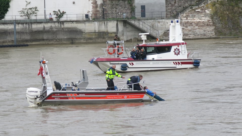 Zwei Rettungskräfte ziehen einen Mann aus dem Rhein, dieser ist beim Hinterteil des Bootes auf einem Brett angemacht.