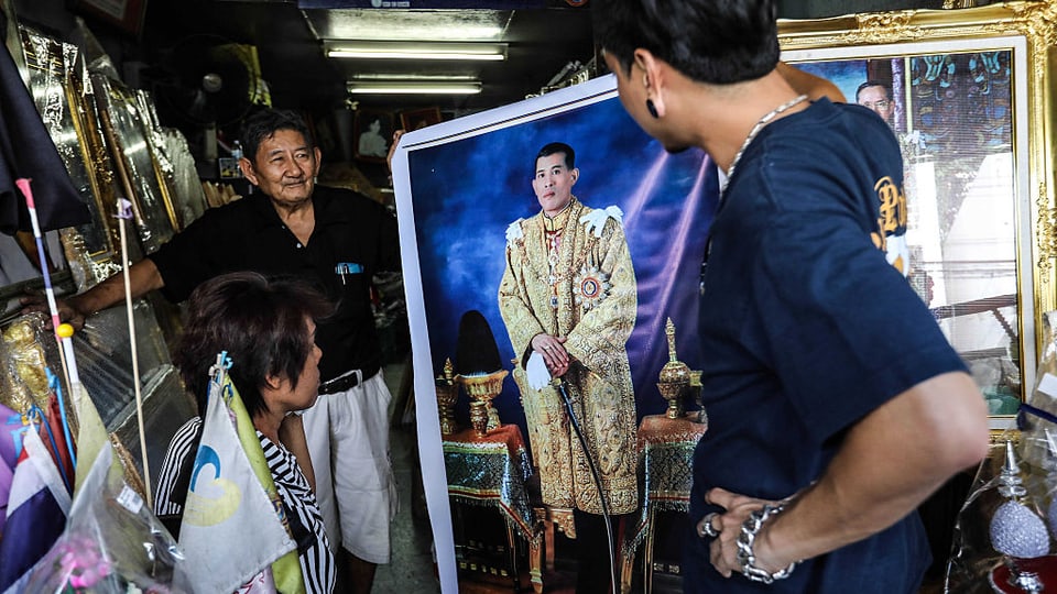 Drei Personen sehen sich in einem Geschäft ein grosses Porträt-Bild Vajiralongkorns an.