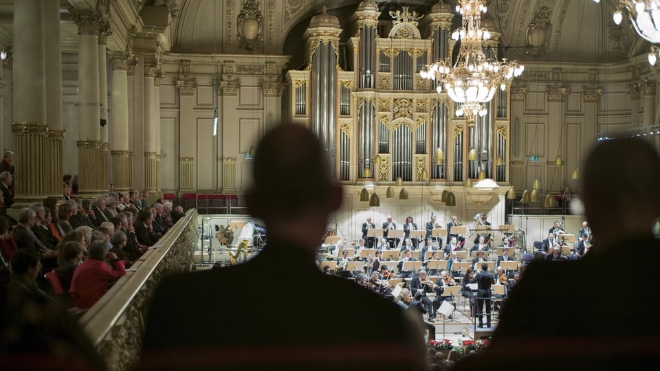 Orchester spielt in einem eleganten Saal mit Zuschauern.