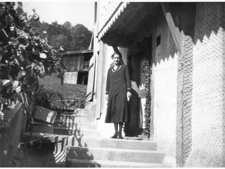 Schwarzweiss-Fotografie einer Frau auf der Treppe vor einem Haus. 