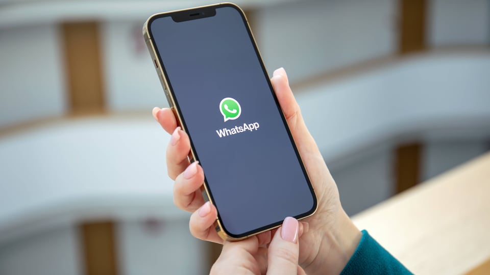 Two hands holding a smartphone, green WhatsApp logo on screen, black background