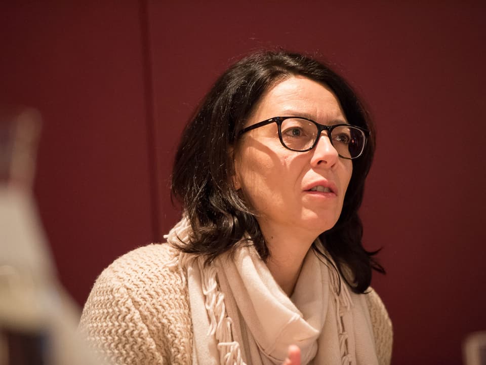 Eine Frau mit weissem Pullover und dunkler Brille, konzentriert.