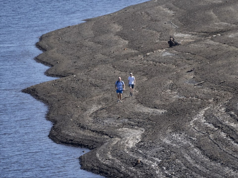 Zwei Personen laufen auf dem trocken gefallen Ufer. 