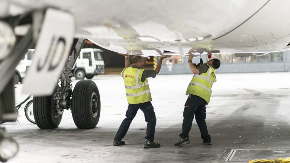 Bodenpersonal der Swiss repariert etwas auf der Flugzeugunterseite.