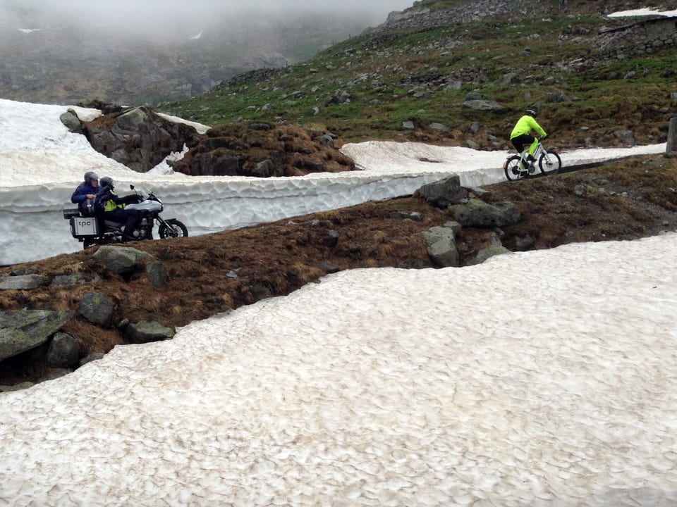 Motorrad folgt Velofahrer durch Schneelandschaft.